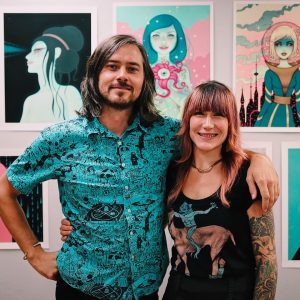 Sean Leonard and Tara McPherson -- A man and a women standing in front of colorful prints hanging on the wall