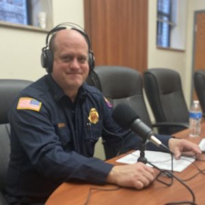 Fire chief sits at desk with headphones in front of a microphone.