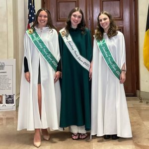 three young women in green and white gowns and sashes smile in a photo