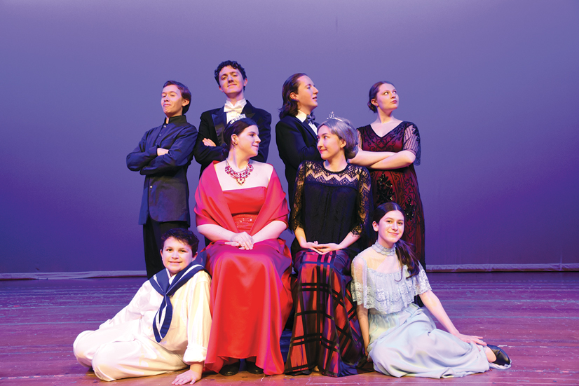 A cast of men in women in costumes on a stage posing for the highschool musical Anastasia