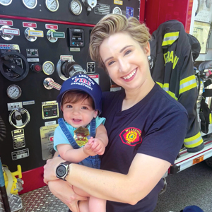 A woman wearing a fire department shirt holding a baby in a fire station