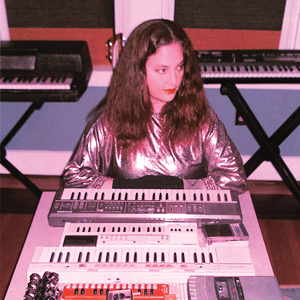 A woman with brown hair sitting at a table with keyboards and music equipment surrounding her