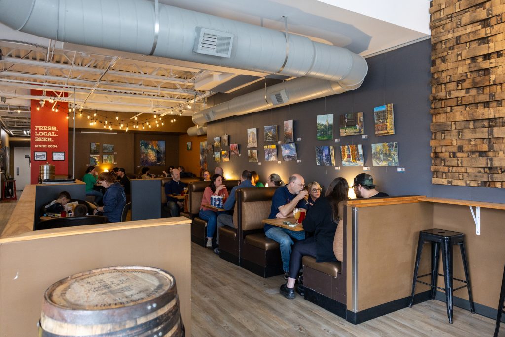 inside of a restaurant and bar with brick walls, wood floors, and people at tables and booths