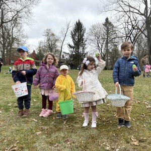 five children holding baskets in a park, two holding green plastic eggs