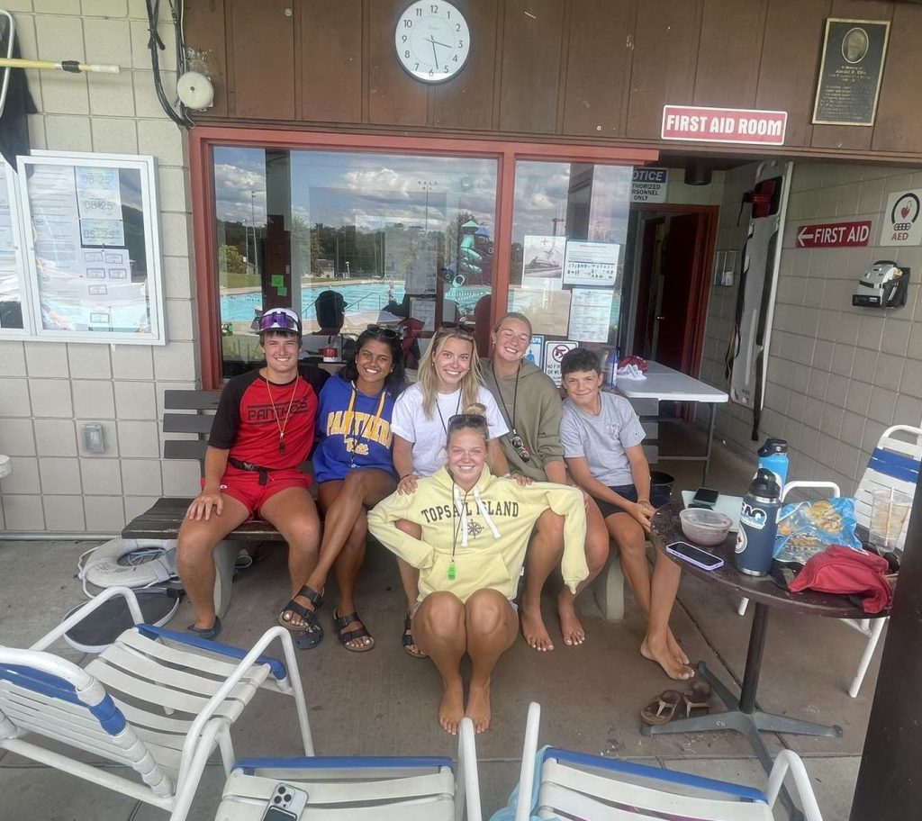 six teens smile for a photo near the break room of a public swimming pool