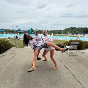 two teen girls holding up a teen boy in white t-shirts at a public swimming pool