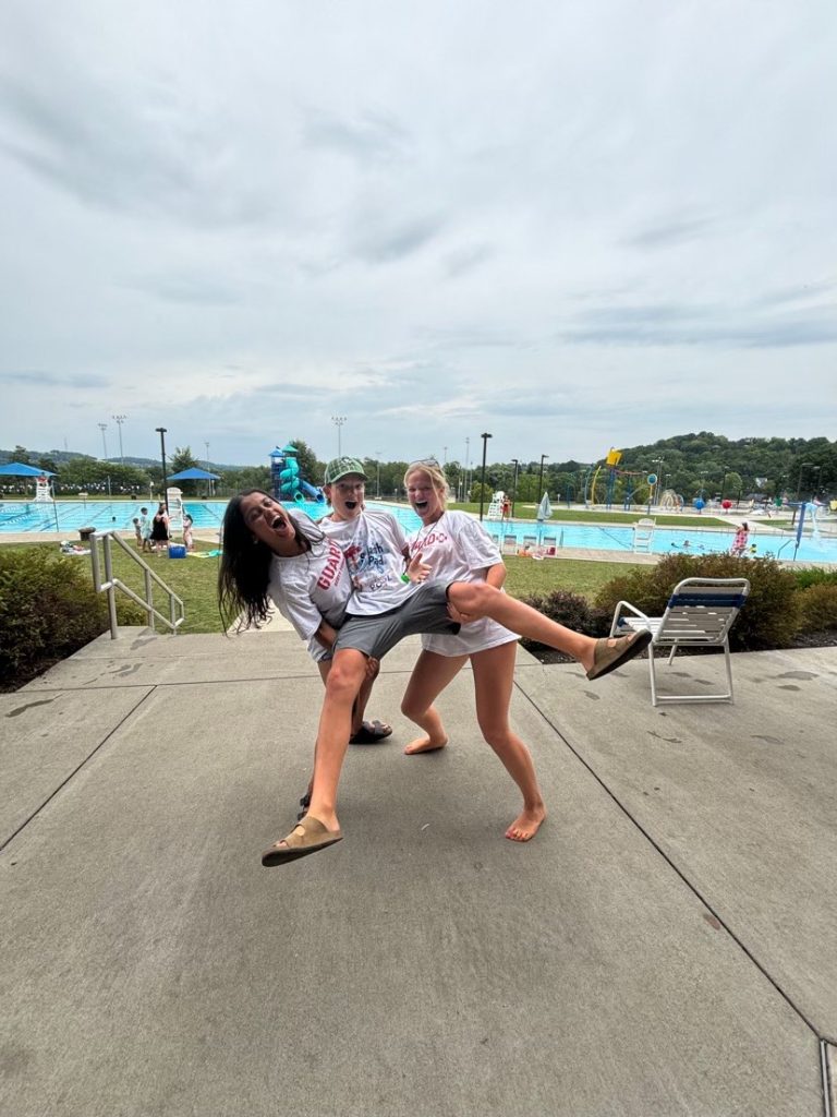 two teen girls holding up a teen boy in white t-shirts at a public swimming pool
