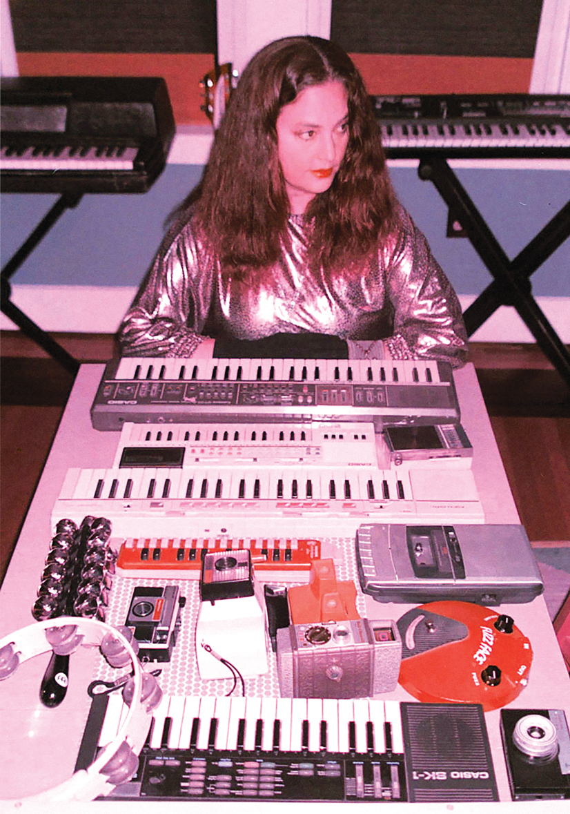 A woman with brown hair sitting at a table with keyboards and music equipment surrounding her