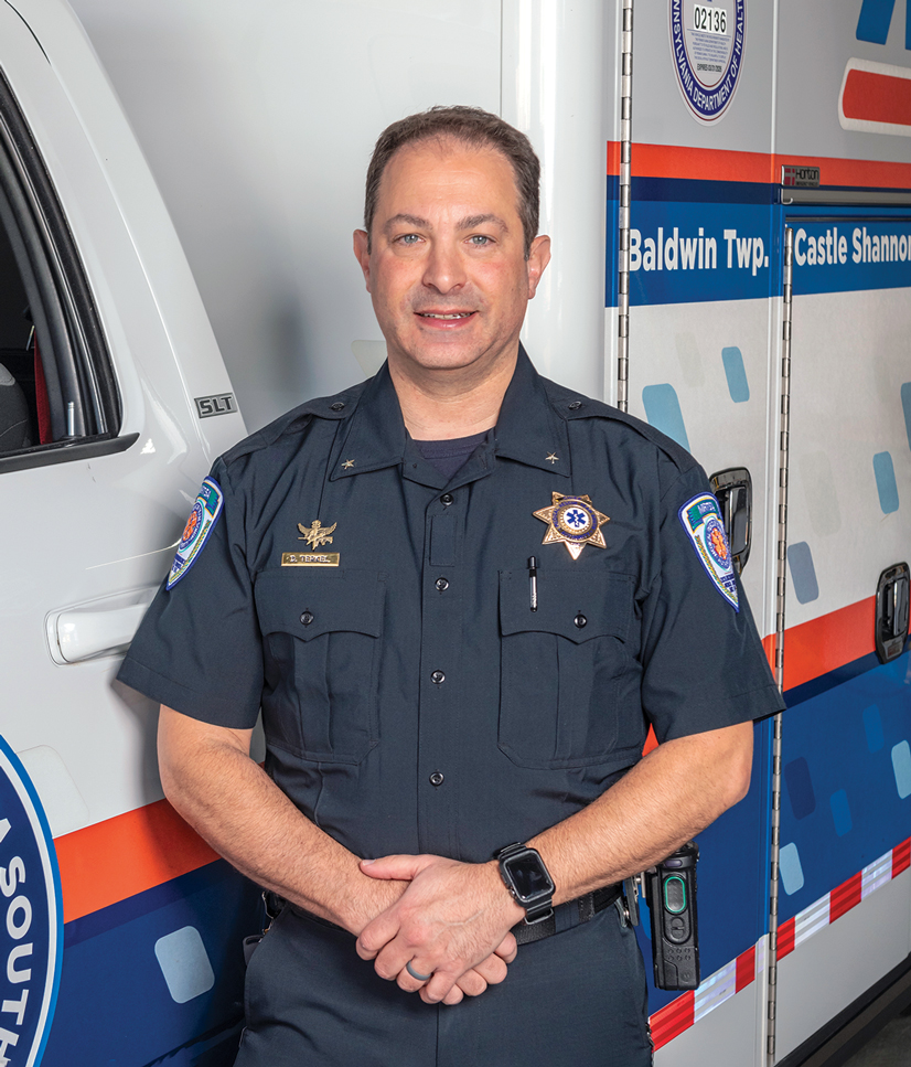 A man wearing a paramedic uniform standing next to an ambulance smiling