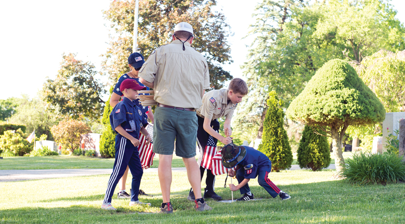 An adult boy scout with 4 kids putting flags in the ground at graves for memorial day