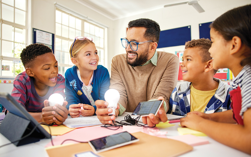 an adult and four school age kids working with gadgets at a desk making light bulbs light up