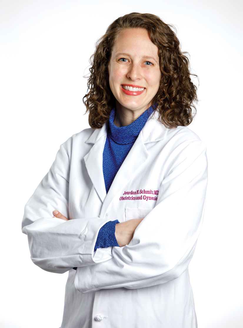 A woman with brown hair wearing a Doctors coat smiling and crossing her arms