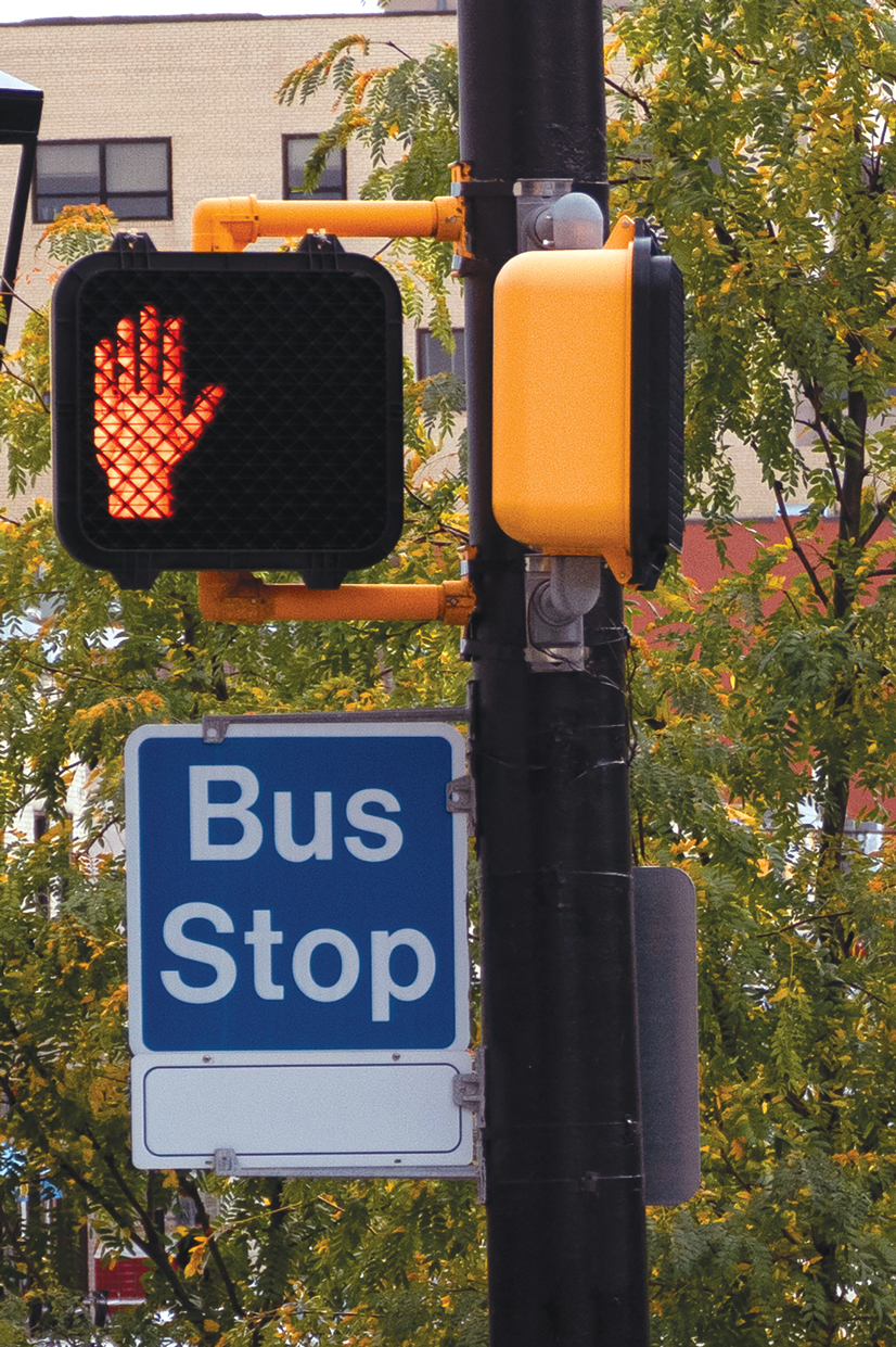 a cross walk light next to a bus stop sign