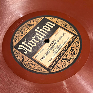 Close up shot of a red vintage record with an ornate gold design in the center.