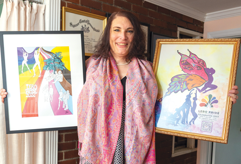A woman wearing a pink scarf holding two frames with colorful Lebo Pride artwork in them