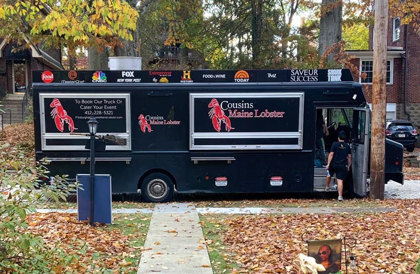 The Cousins Maine Lobster truck on the side of the street in the fall, leaves are all over the ground