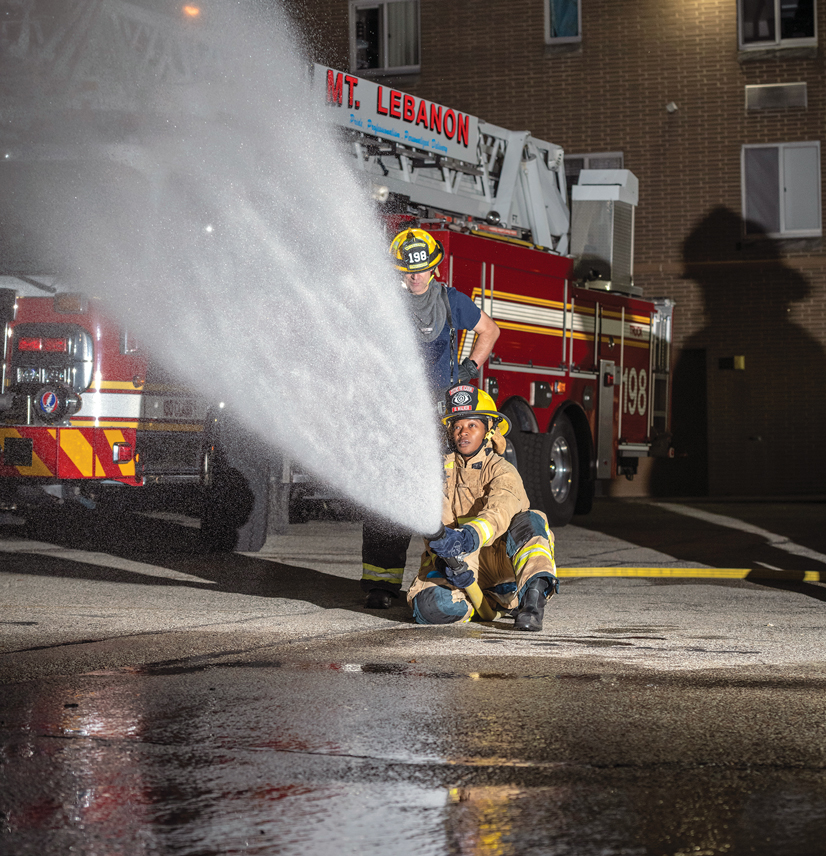 two people in firefighter gear spraying a firehose