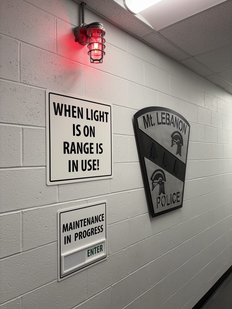 white wall with Mt. Lebanon police logo, red light, and signs for gun range