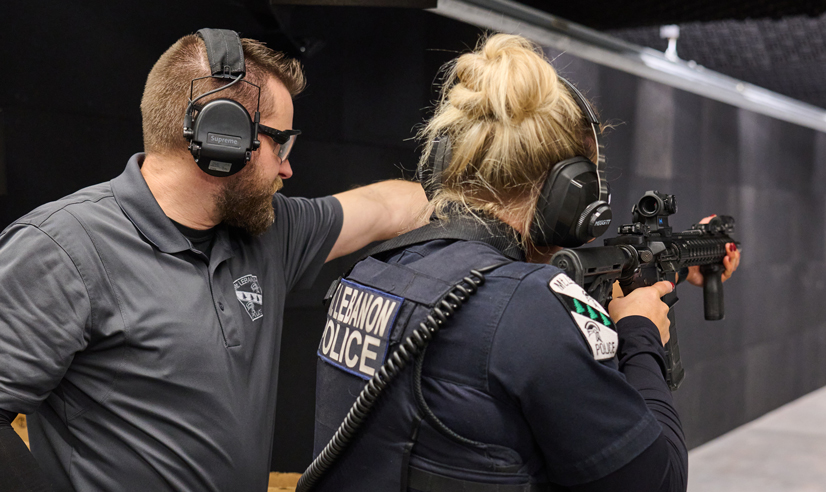 A man pointing down the firing range standing next to a woman police officer holding a gun