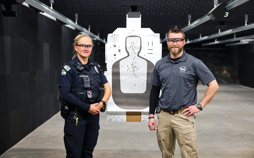 A man and a woman police officer standing next to a target full of bullet holes