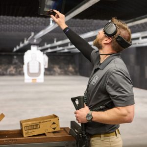 A man holding a rifle, pushing a button to move the target back
