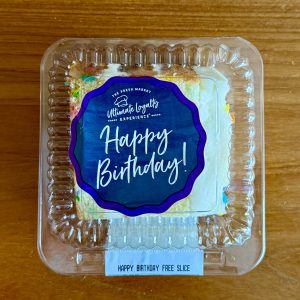 cake slice in plastic container with sticker that says happy birthday