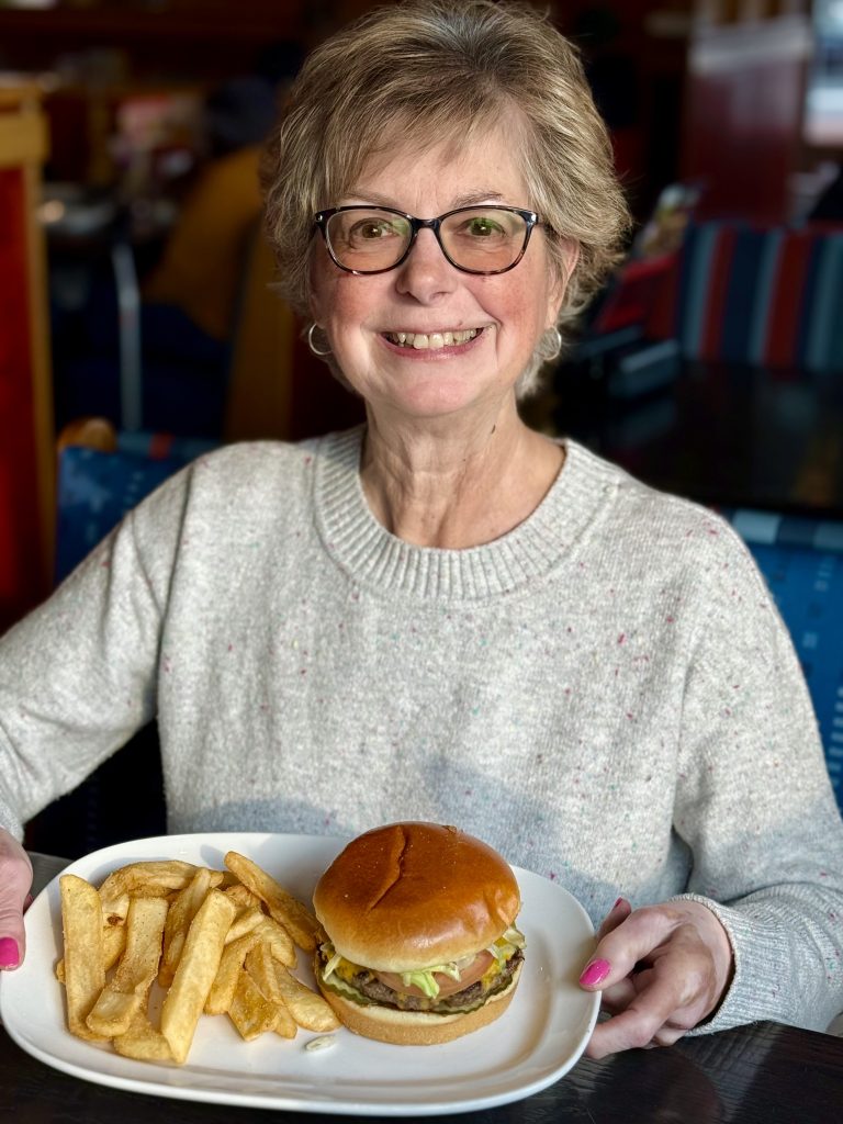 woman smiling with glasses holding a plate with a burger and fires