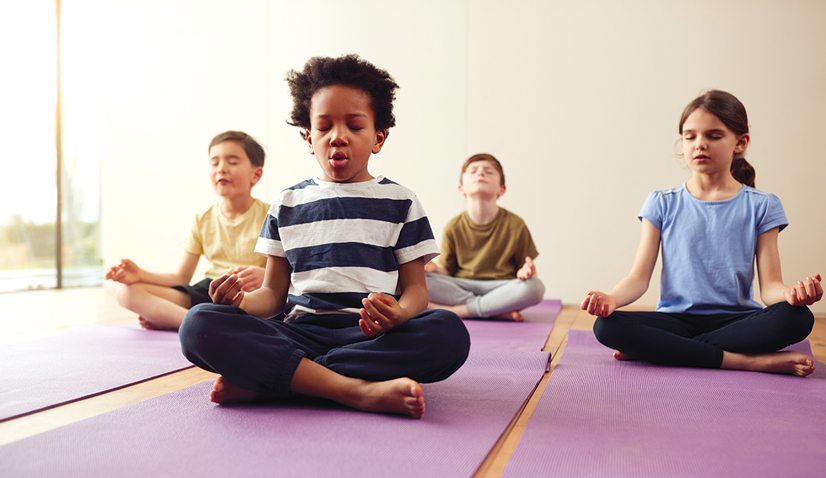 four children sitting in yoga pose on purple mats