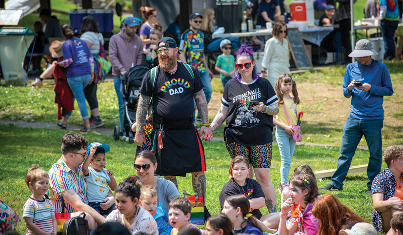 Two people holding hands standing in a crowd near a bunch of people sitting down