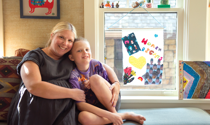 A mom and child sitting together on a bench near a window with artwork on it that says "women rights"