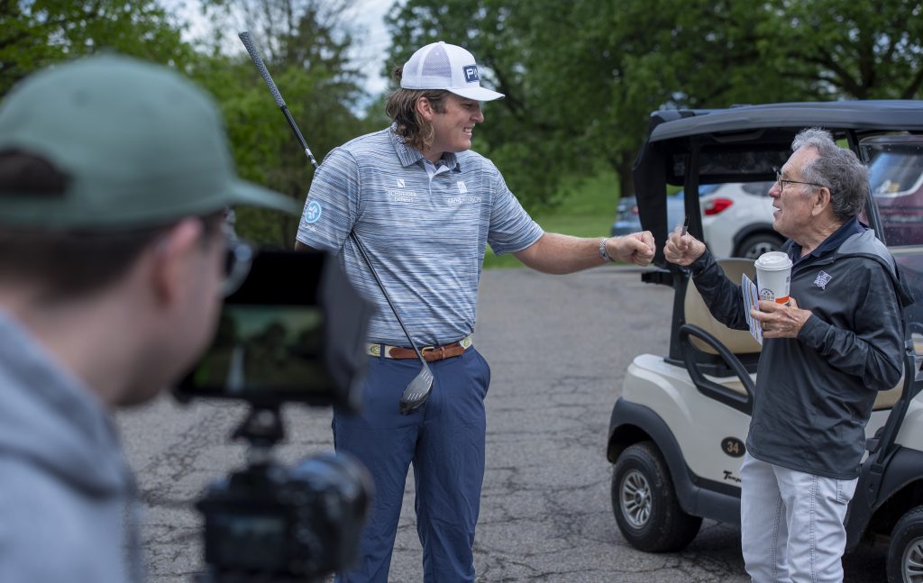 camera man filming a golfer with a white hat and an elderly man fist bumping