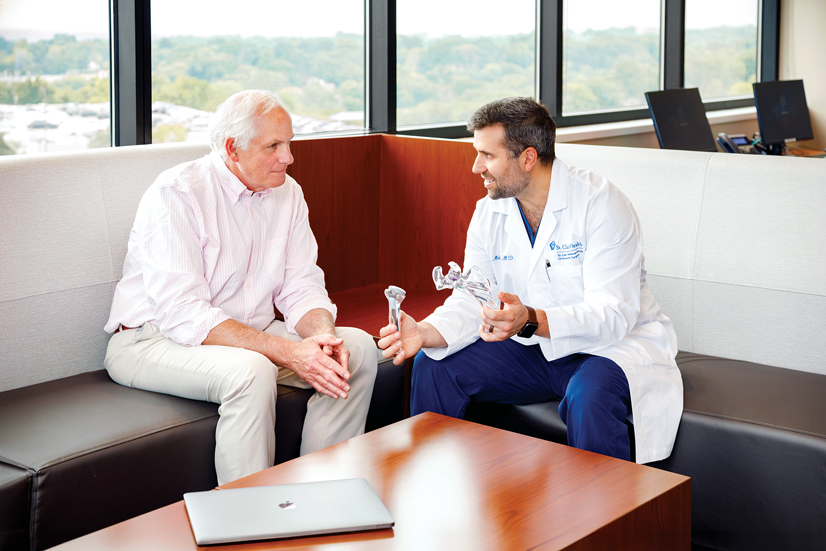 A man and a doctor sitting at a table talking, the doctor is holding plastic tools