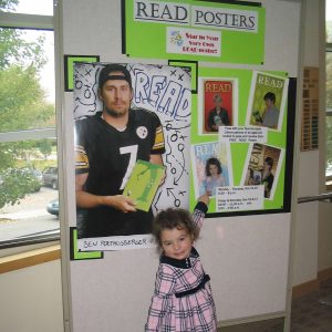 toddler in pink dress points to a billboard for reading