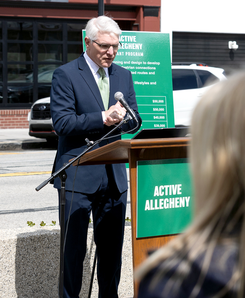 man in suit at podium with white hair and green signs