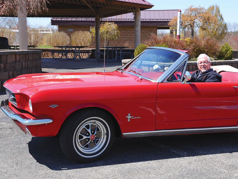 A man with glasses sitting in his red 1964 convertable mustang with the top down