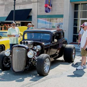three men looking at a black classic car on a sunny day at a car show