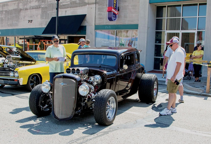 three men looking at a black classic car on a sunny day at a car show