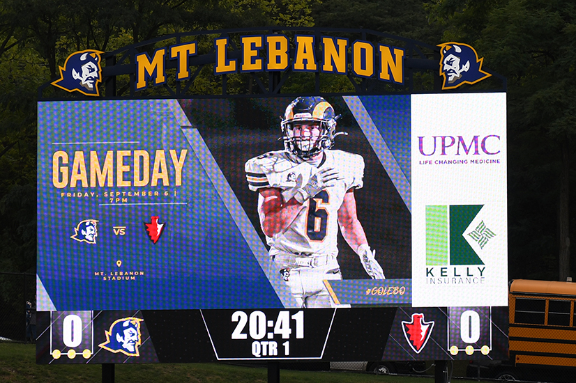 Video scoreboard with "Mt. Lebanon" spelled out in large yellow block letters at the top. The word "Gameday" with a blue devil and a red arrowhead logo, a football player image, and first quarter score tied at 0-0, time 20:41.