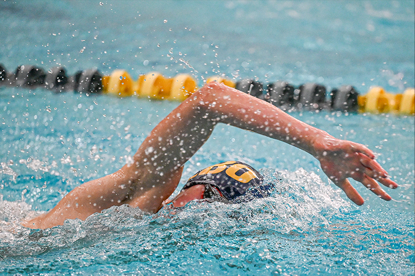 A swimmer in a blue cap with large yellow letters in a pool, splashing water.