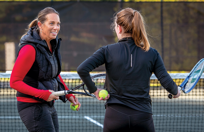 two women interacting on tennis court in winter clothing