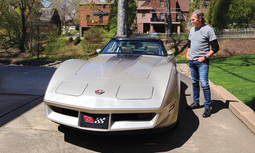 A man standing next to his silver 1982 corvette in his driveway