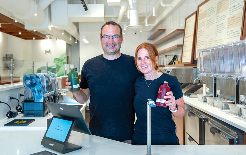 man and woman hold colorful juice bottles in a health food store