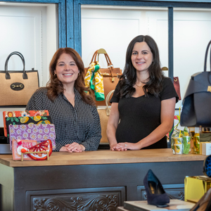 two women in dresses smile in a shoe boutique