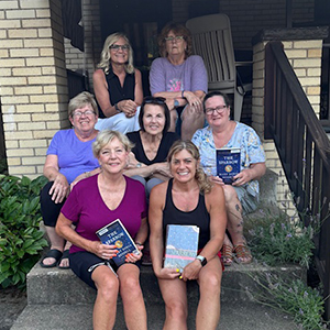 women sit on the steps of a house holding a book
