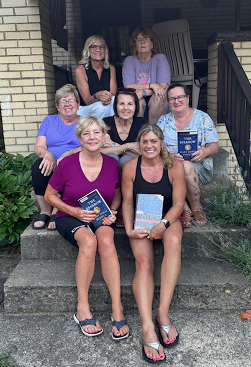 women sit on the steps of a house holding a book