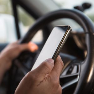 The driver's hand behind the wheel holds a smartphone. Navigator, satellite navigation, communication in the car, road safety, speakerphone