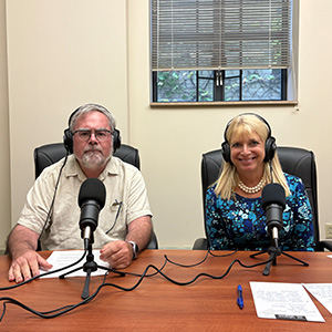man and woman with headphones on sitting at a table with microphones