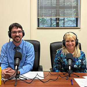 Ian McMeans and Laura Pace Lilley with headphones on, in front of microphones.