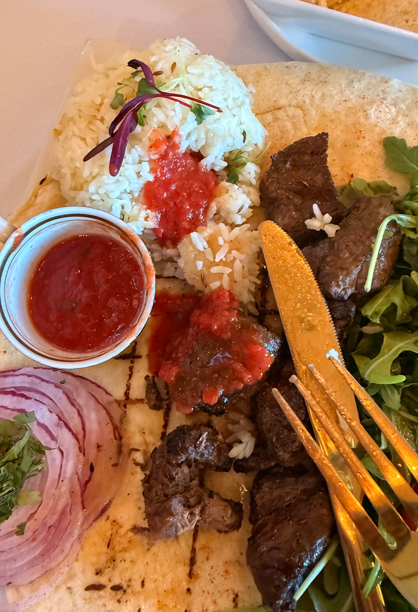 plate of food with onions, meat, red sauce, rice and gold fork and knife