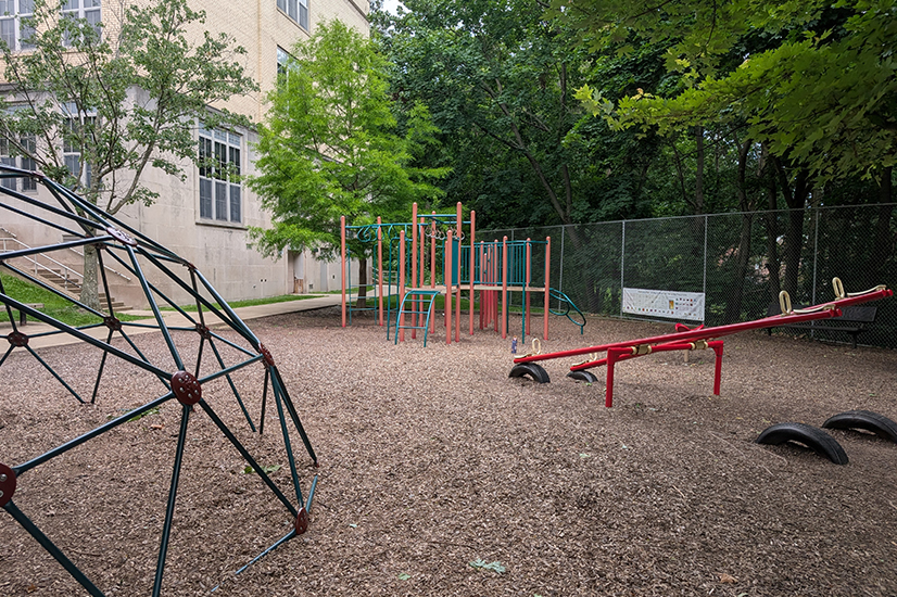 playset with see-saw and climbing bars on wood chips with building in background